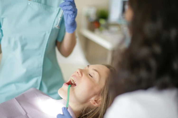 Experienced implant dentists preparing to inspect patient’s teeth with assistant holding suction tube