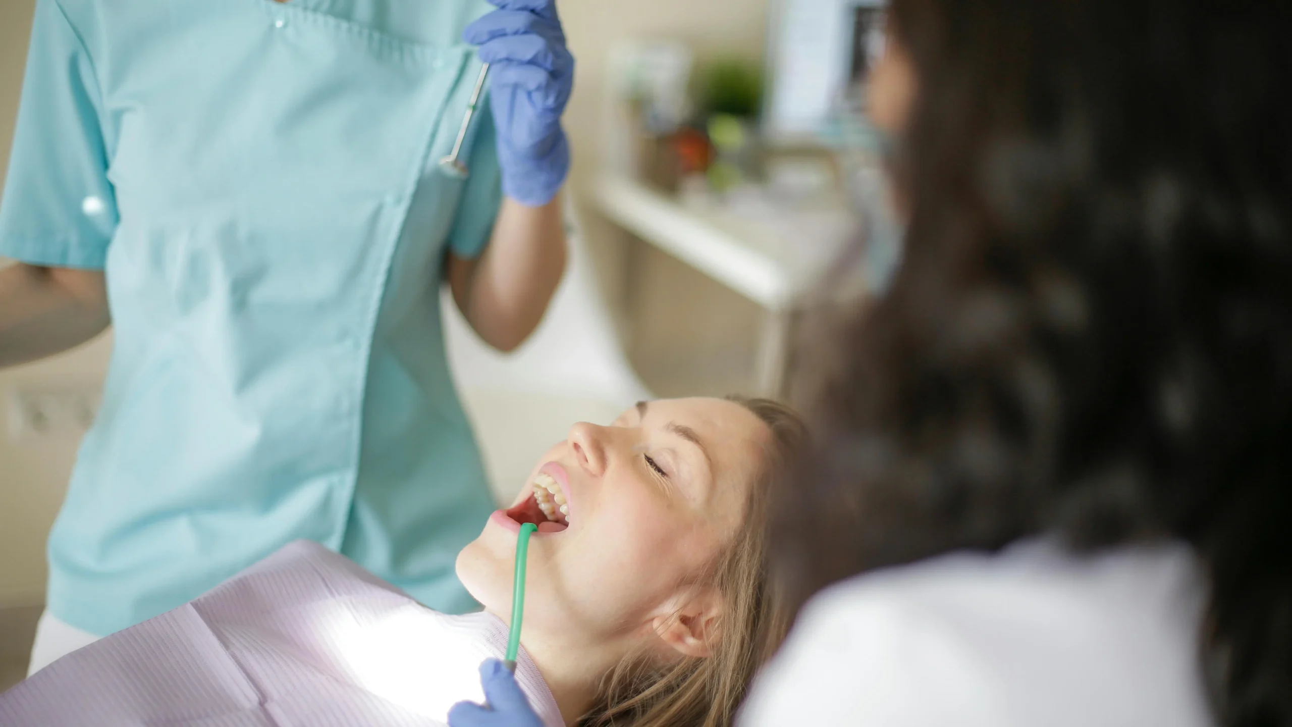 Experienced implant dentists preparing to inspect patient’s teeth with assistant holding suction tube