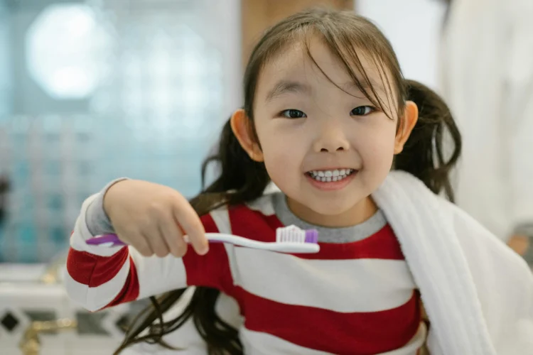 Cheerful child brushing teeth with help from child dental care specialist