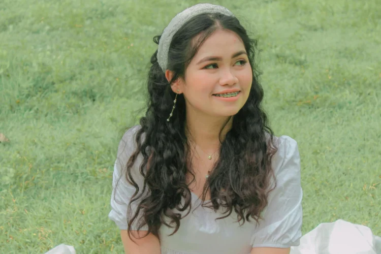 Young woman smiling in a white dress, showcasing clear braces with Invisalign