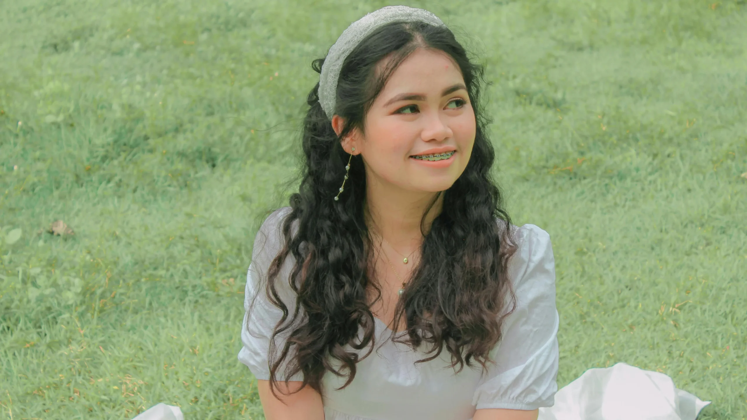 Young woman smiling in a white dress, showcasing clear braces with Invisalign