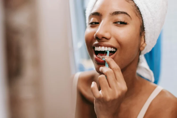 Smiling African American woman using dental flosser, emphasizing full mouth dental implants