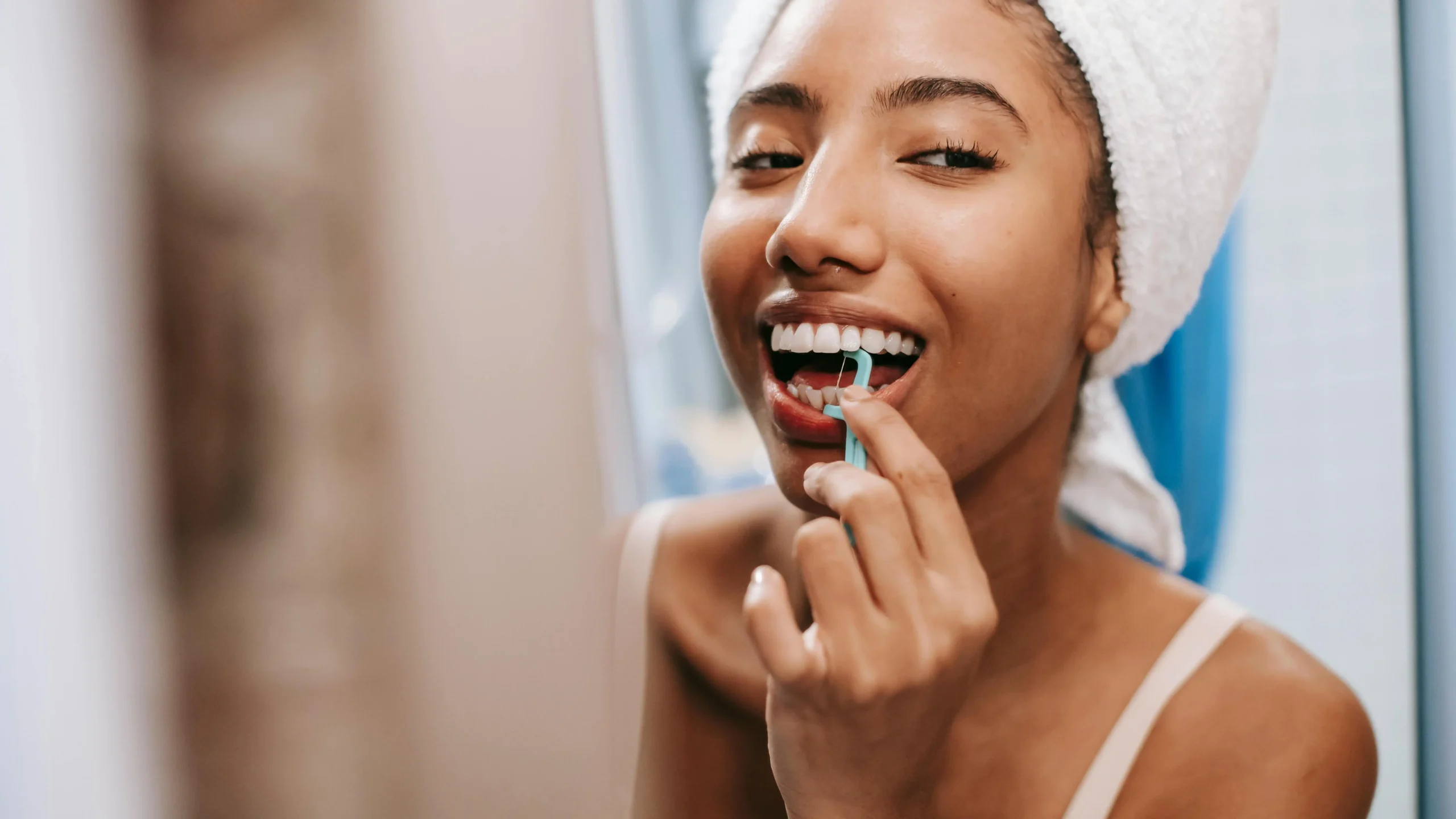 Smiling African American woman using dental flosser, emphasizing full mouth dental implants