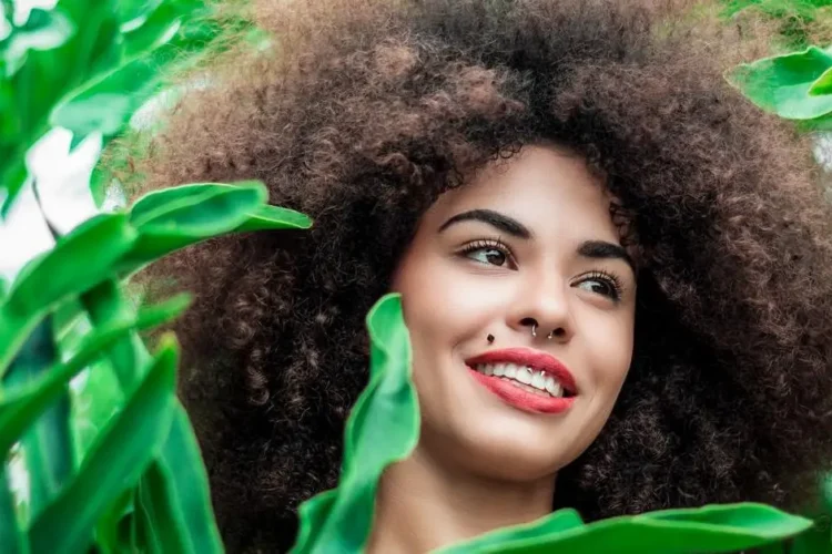 Smiling woman promoting at home teeth whitening surrounded by green plants.