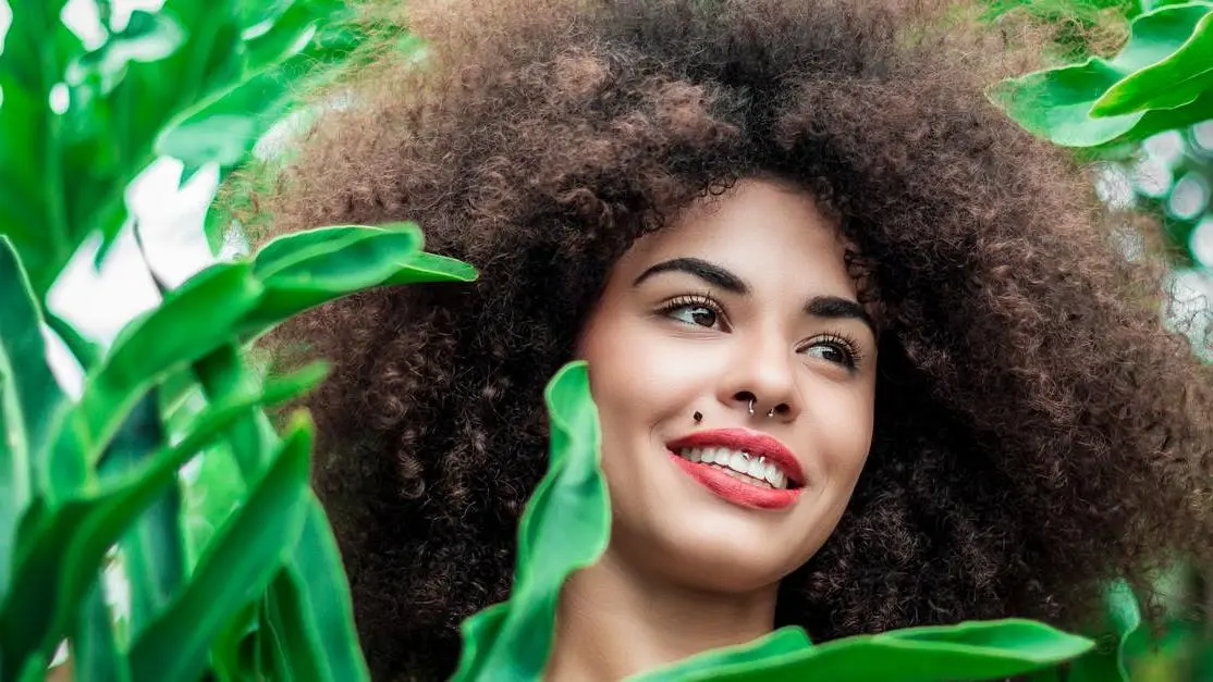 Smiling woman promoting at home teeth whitening surrounded by green plants.