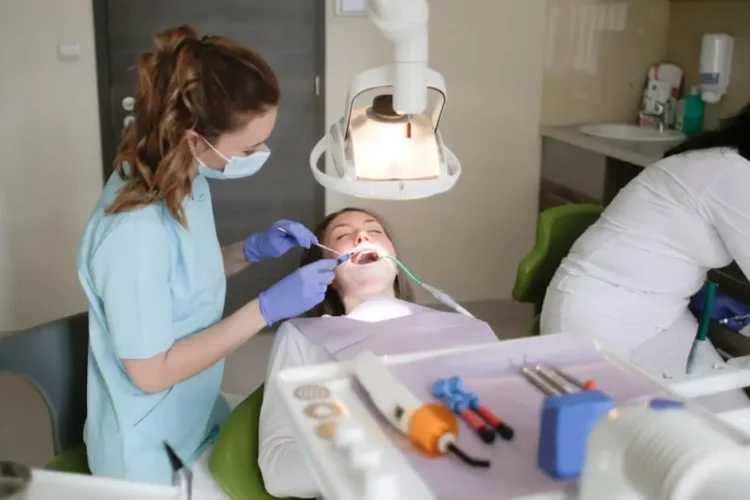 Caregiver in blue scrubs examining patient's teeth for dental health