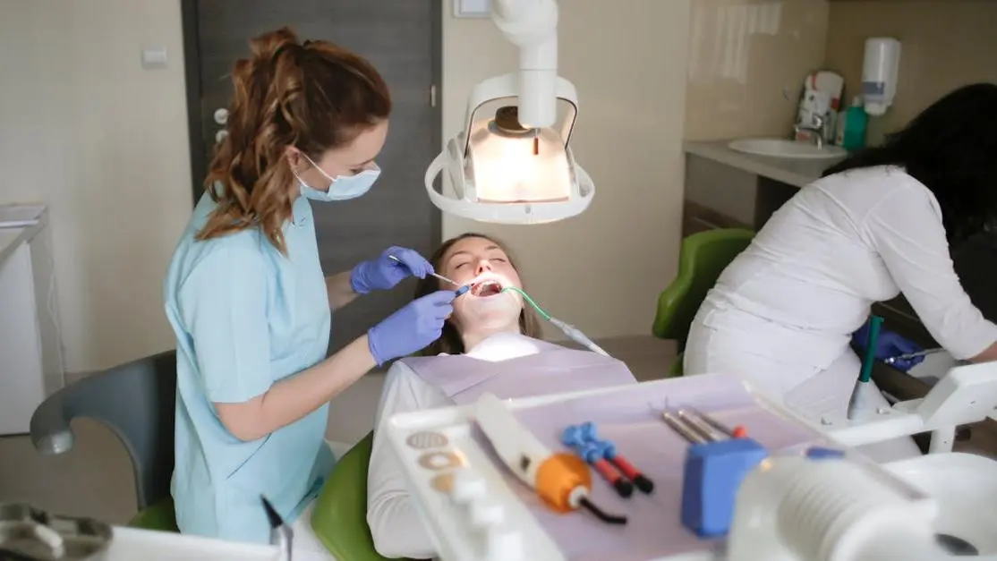 Caregiver in blue scrubs examining patient's teeth for dental health