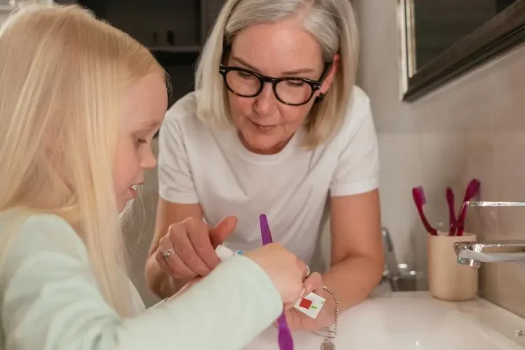 Grandmother guiding granddaughter in brushing for dental care for seniors.