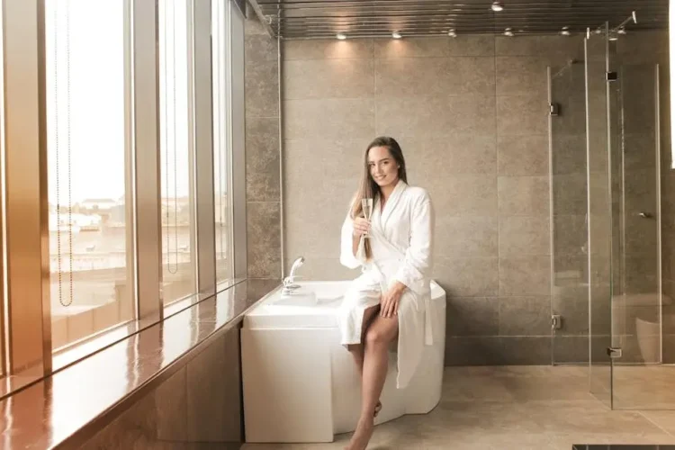 Smiling woman in bathrobe caring for dental veneers while enjoying champagne in bathroom