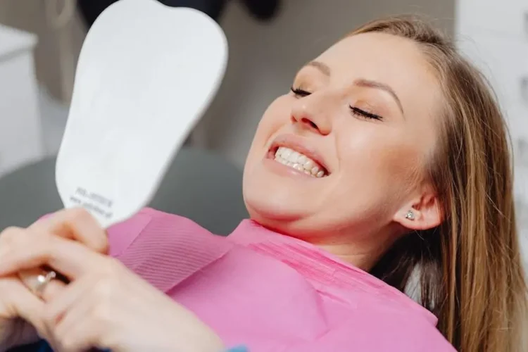 Thrilled patient admiring her smile with experienced cosmetic dentists' work reflected in the mirror.