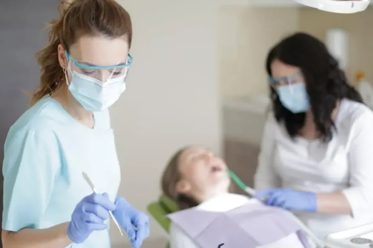 Experienced dental surgeons selecting dental treatment materials while assistant aids patient