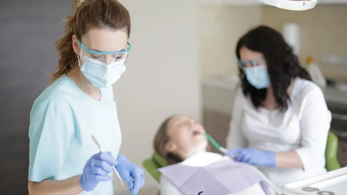 Experienced dental surgeons selecting dental treatment materials while assistant aids patient