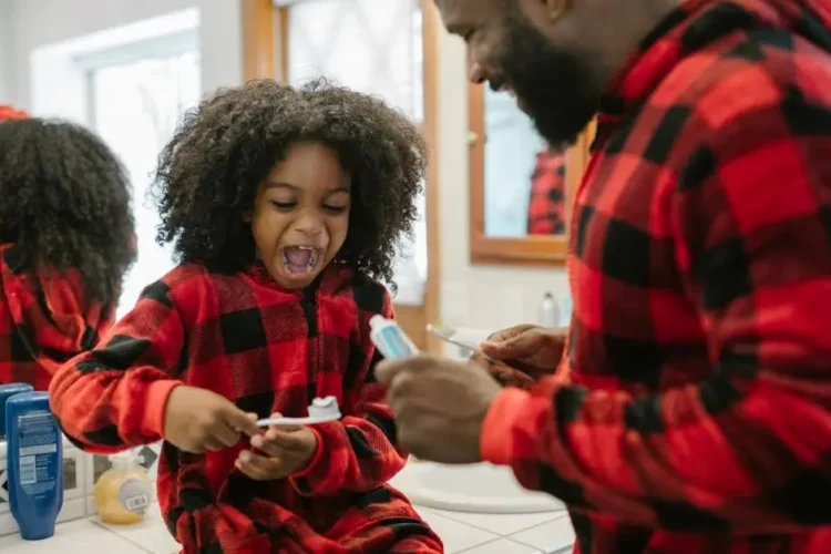 Father and daughter smiling brushing teeth, promoting kids dental care.