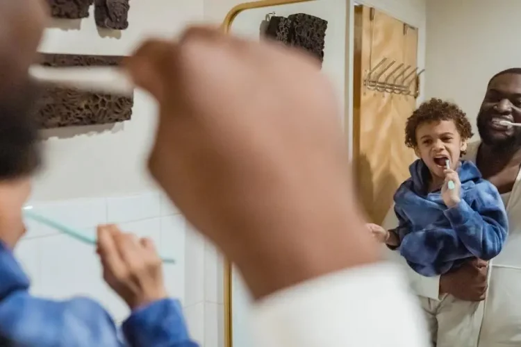 Father and son practicing oral hygiene in bathroom mirror.