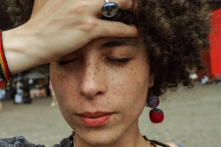 Woman holding her forehead with eyes closed, depicting techniques to reduce dental anxiety.