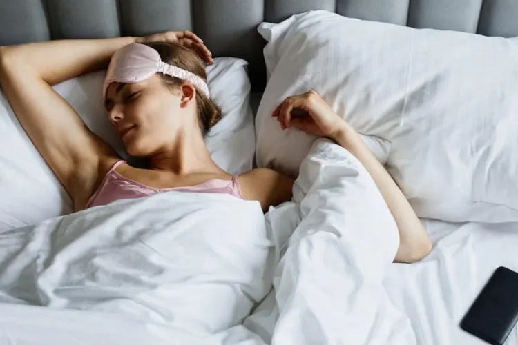 Woman sleeping in bed wearing eye mask, representing sleep dentist for sleep apnea.