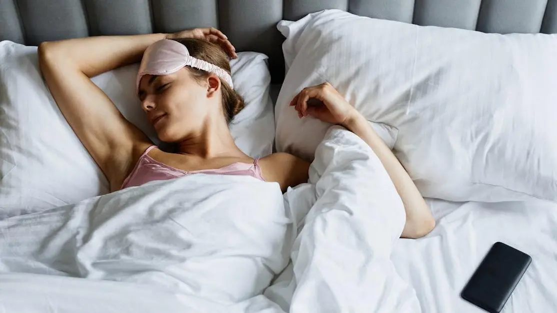 Woman sleeping in bed wearing eye mask, representing sleep dentist for sleep apnea.