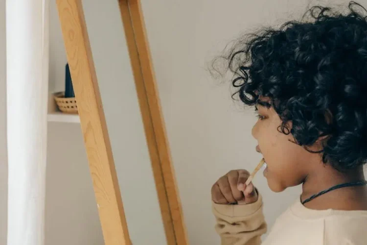 Child brushing teeth in front of mirror to prevent tooth cavities