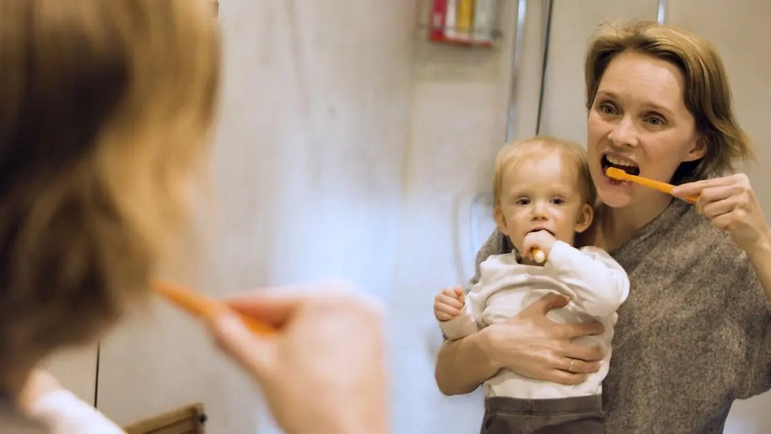 Baby brushing teeth with mother to prevent baby bottle tooth decay.