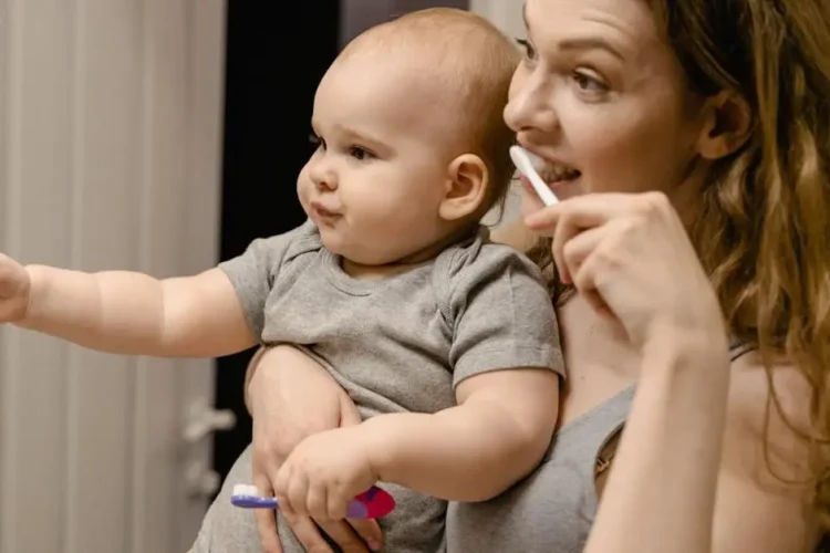 Mother holding baby while brushing teeth, emphasizing daily routine with baby teeth care.