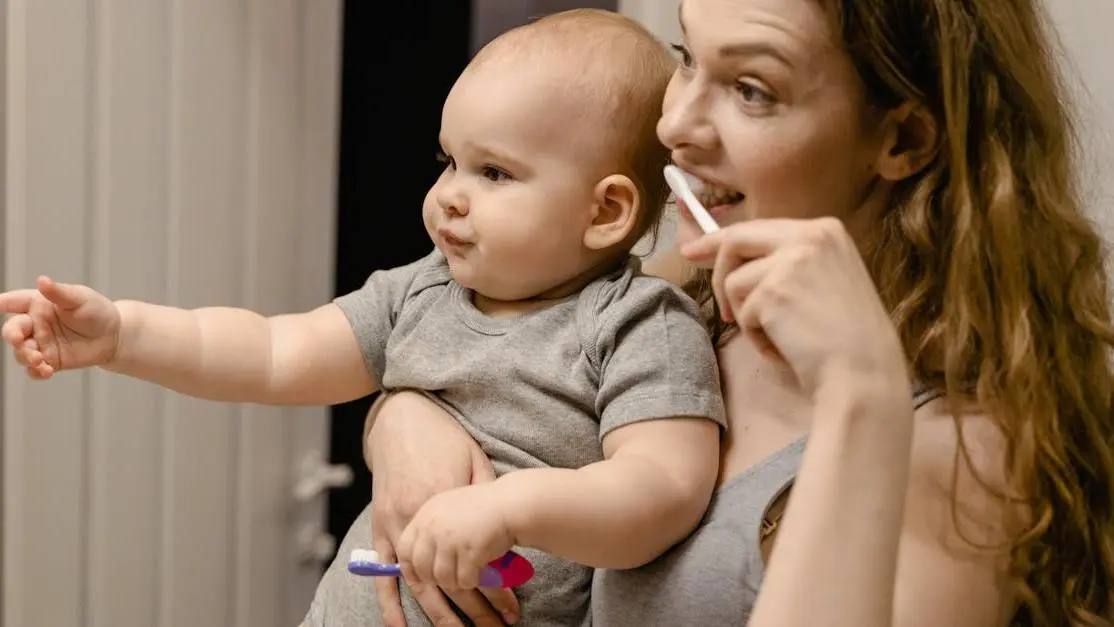 Mother holding baby while brushing teeth, emphasizing daily routine with baby teeth care.