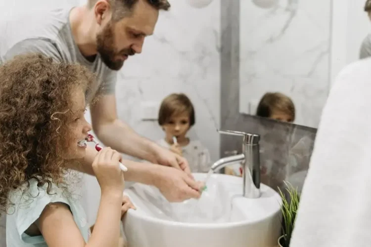 Father and children brushing teeth in bathroom, promoting family dental care for children and adults.