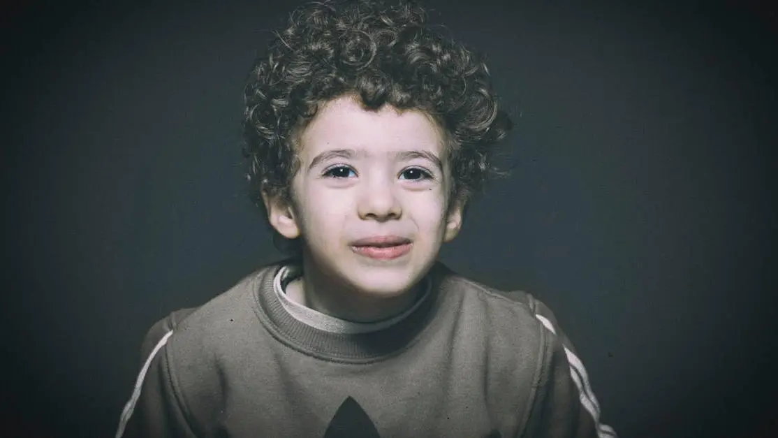 Smiling child with curly hair, representing general dentistry in a studio setting.