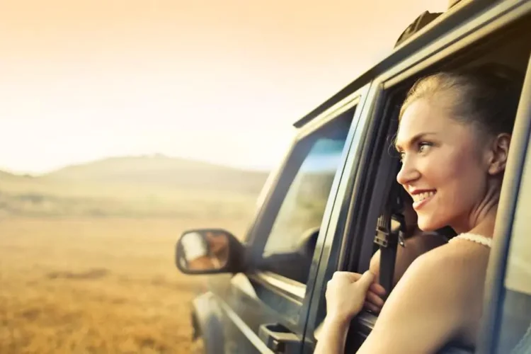 Young woman showing a gummy smile while enjoying a sunset through an open car window.