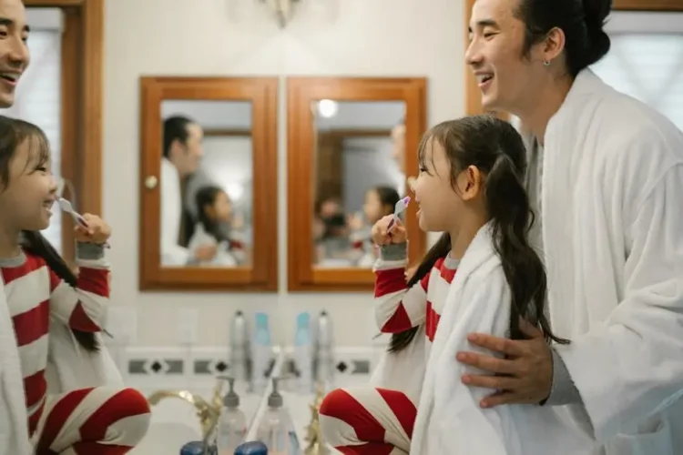 Father assisting daughter with tooth brushing; highlights importance of dental care for kids.