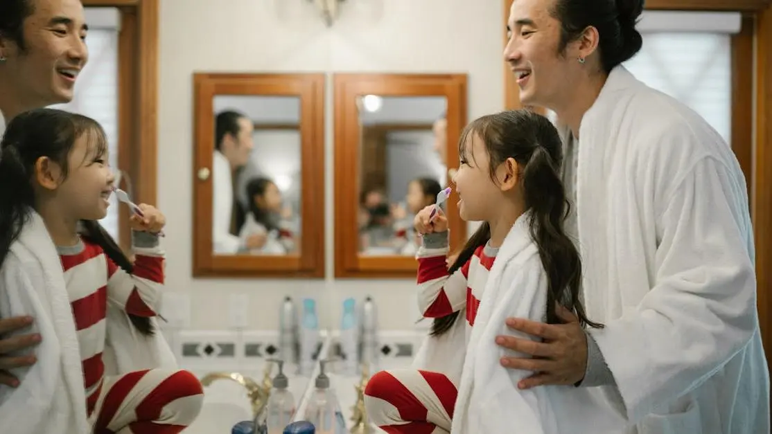 Father assisting daughter with tooth brushing; highlights importance of dental care for kids.