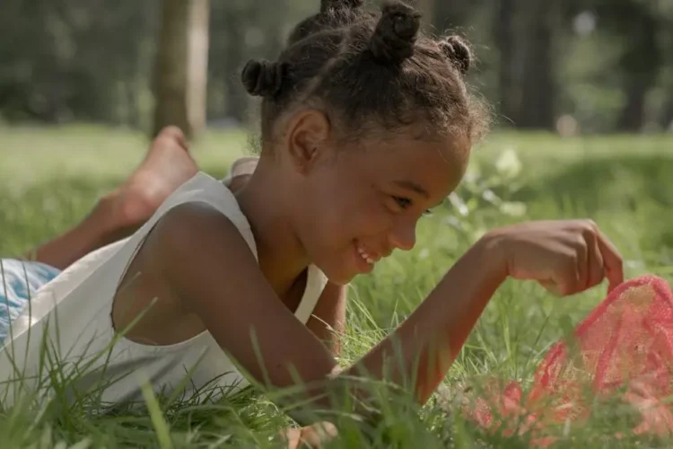 Young girl smiling in a sunny park, highlighting the importance of dental care for kids.