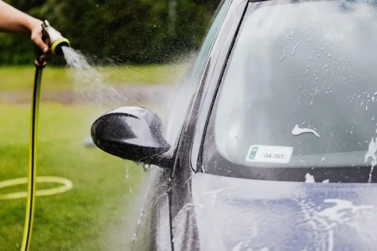 Regular cleaning of a car with a hose, highlighting the importance of regular cleanings.