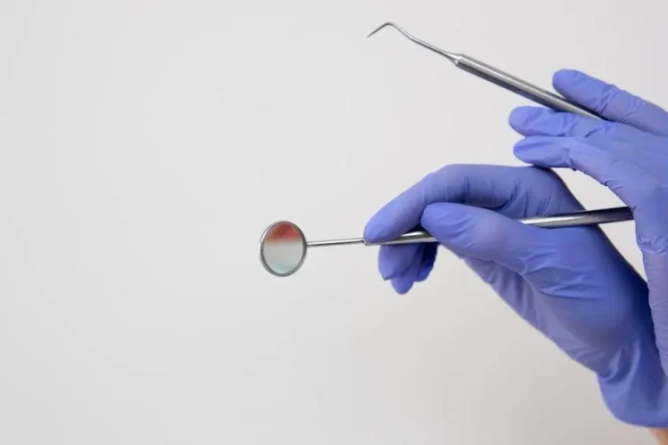 Dentist's gloved hands examining lingual tooth surface with dental mirror and probe.