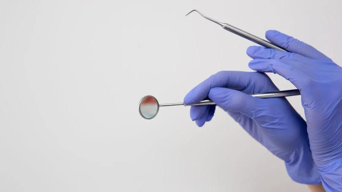 Dentist's gloved hands examining lingual tooth surface with dental mirror and probe.