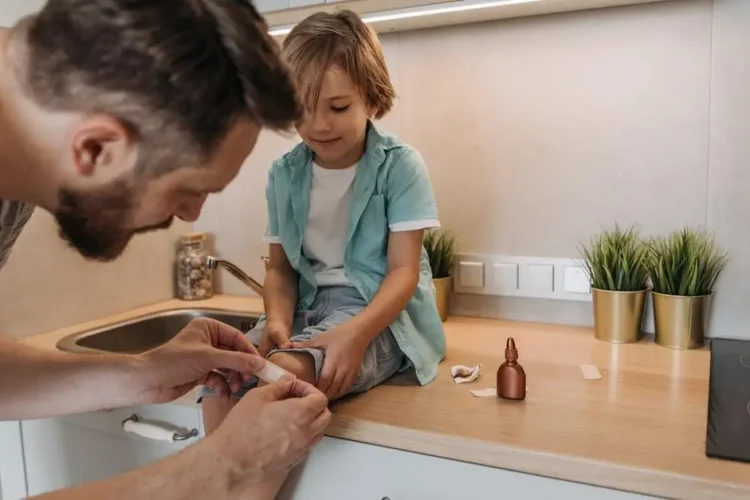 Father bandaging child's knee on kitchen counter, illustrating managing dental emergencies at home.