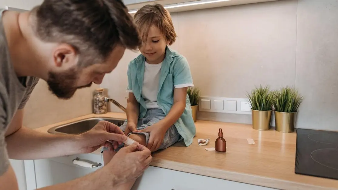 Father bandaging child's knee on kitchen counter, illustrating managing dental emergencies at home.