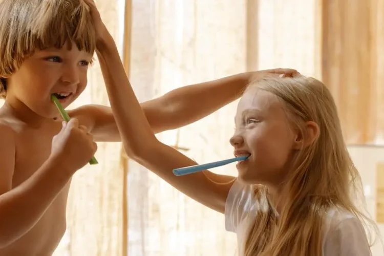 Children practicing oral hygiene tips for kids, brushing teeth in a sunlit bathroom.