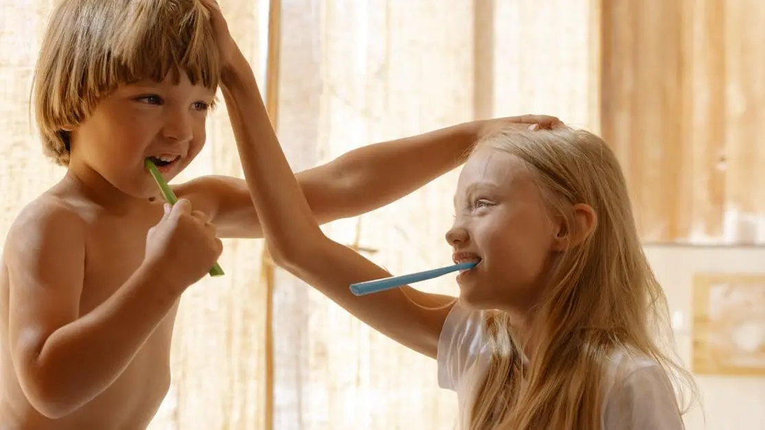 Children practicing oral hygiene tips for kids, brushing teeth in a sunlit bathroom.