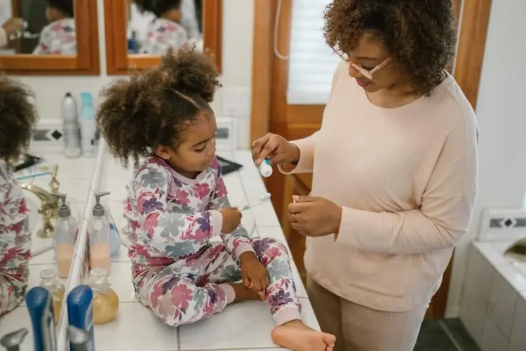 Child brushing teeth under mother's supervision, illustrating sugar impact on children's teeth.