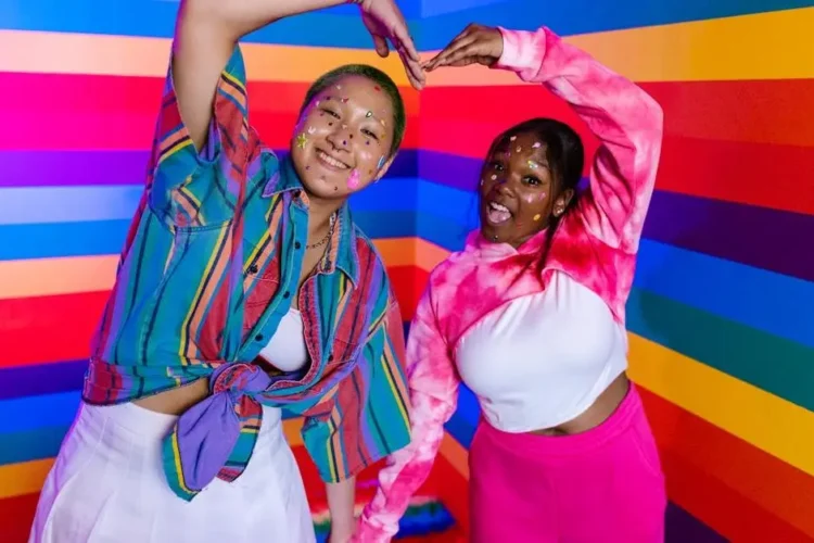 Two women smiling against rainbow backdrop, representing inclusivity and happiness, related to teeth whitening options near me.