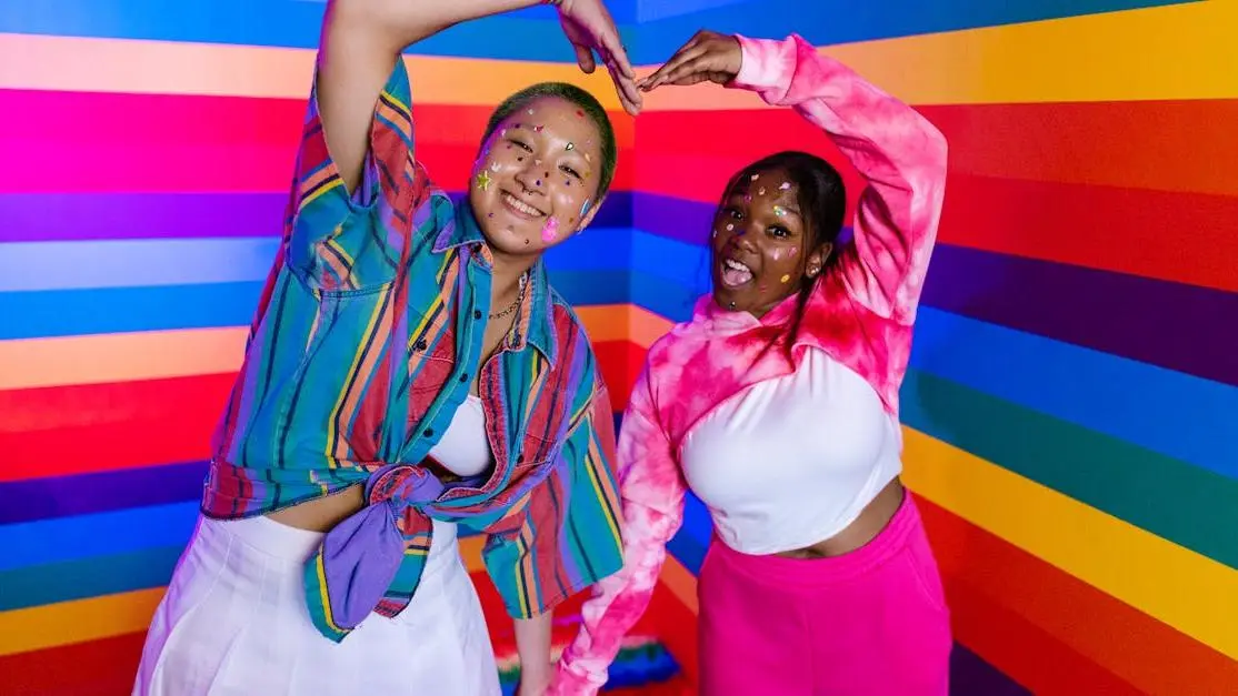 Two women smiling against rainbow backdrop, representing inclusivity and happiness, related to teeth whitening options near me.